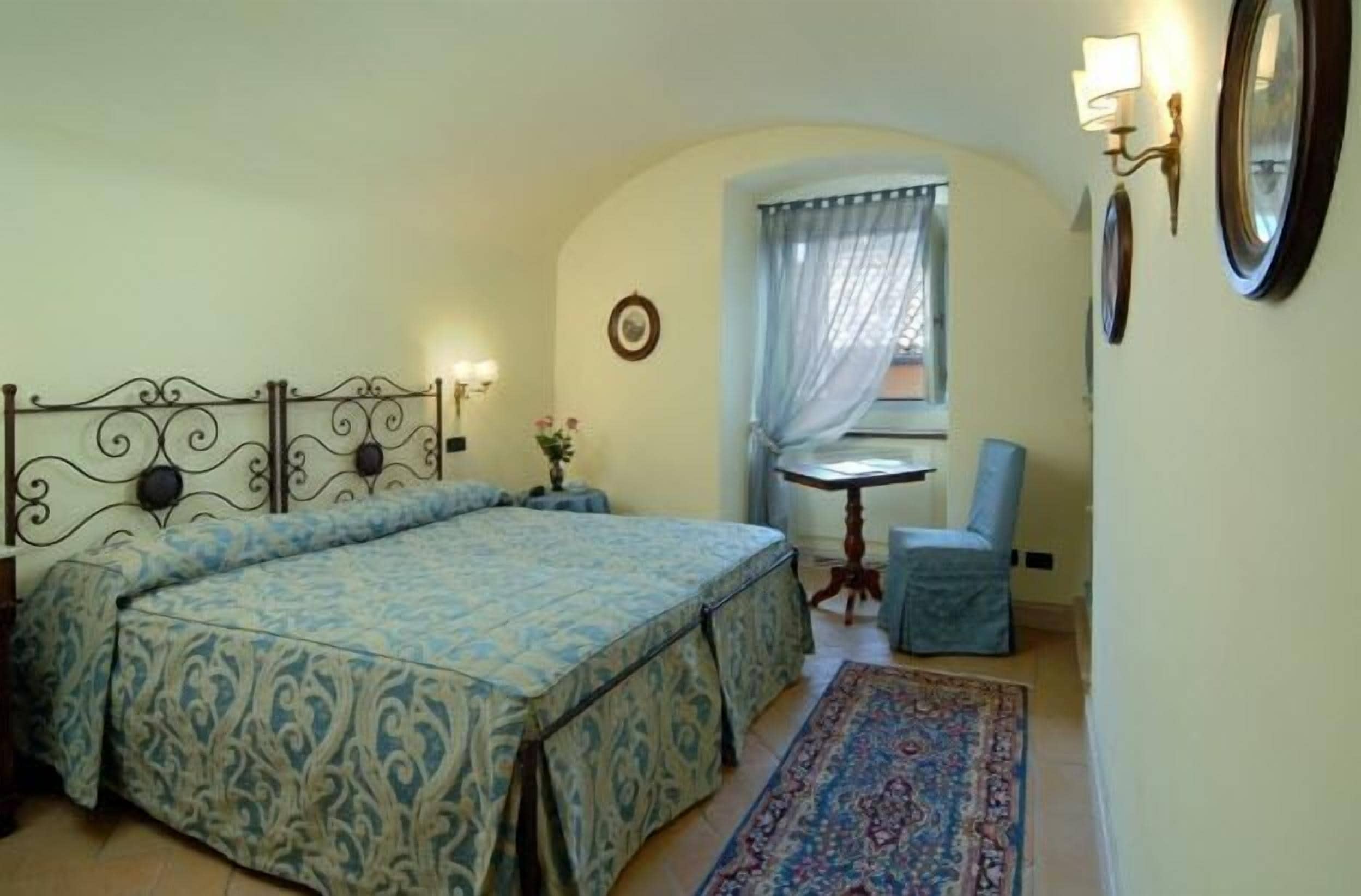 Un dormitorio con una cama doble, una mesita pequeña, una silla y una ventana con cortinas.