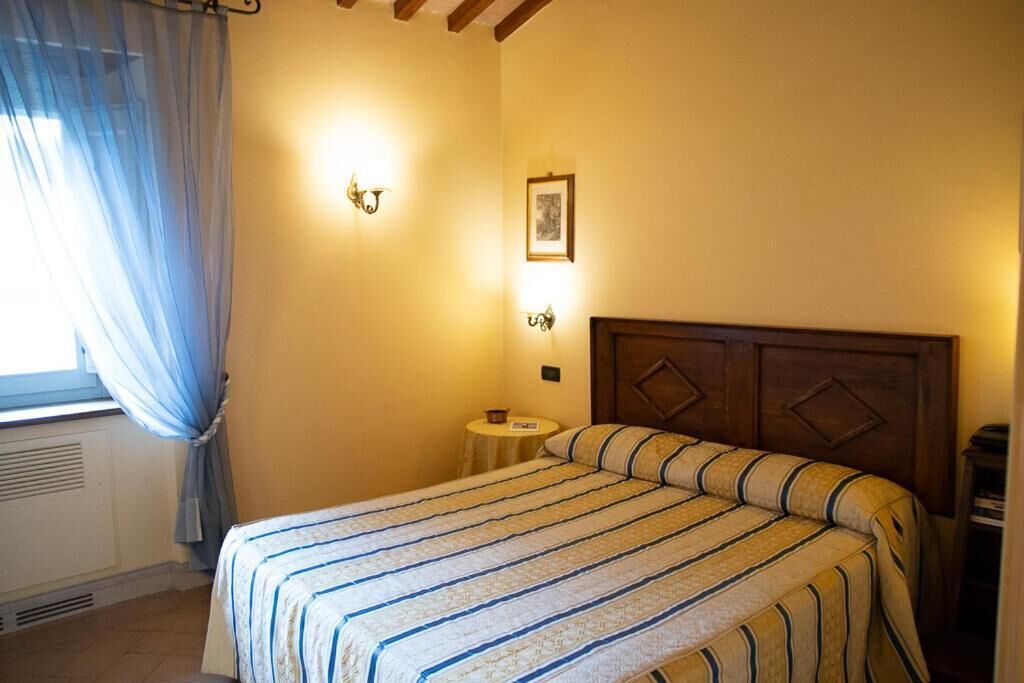 A bedroom with a bed, a bedside table, a nightstand, a window with curtains, and wall-mounted lights.