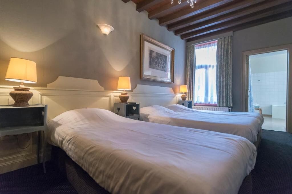 A hotel room with two beds, bedside lamps, a framed picture on the wall, and a window with curtains.