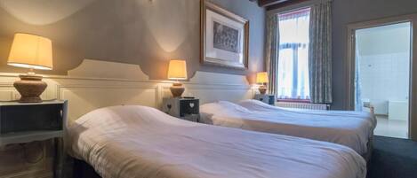 A hotel room with two beds, bedside lamps, a framed picture on the wall, and a window with curtains.