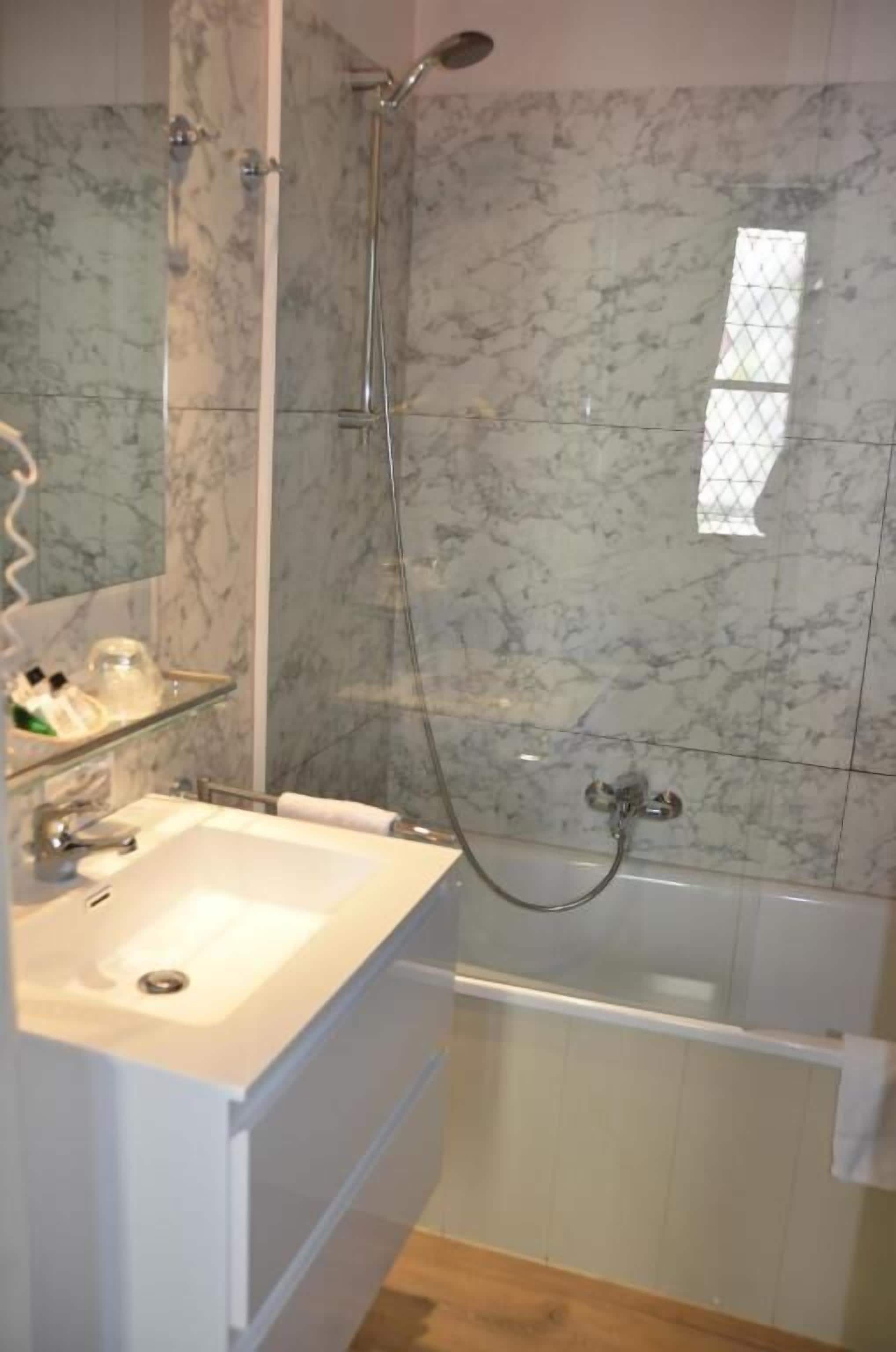 Une salle de bain avec un mur en marbre, un lavabo blanc, une douche en verre et une baignoire.