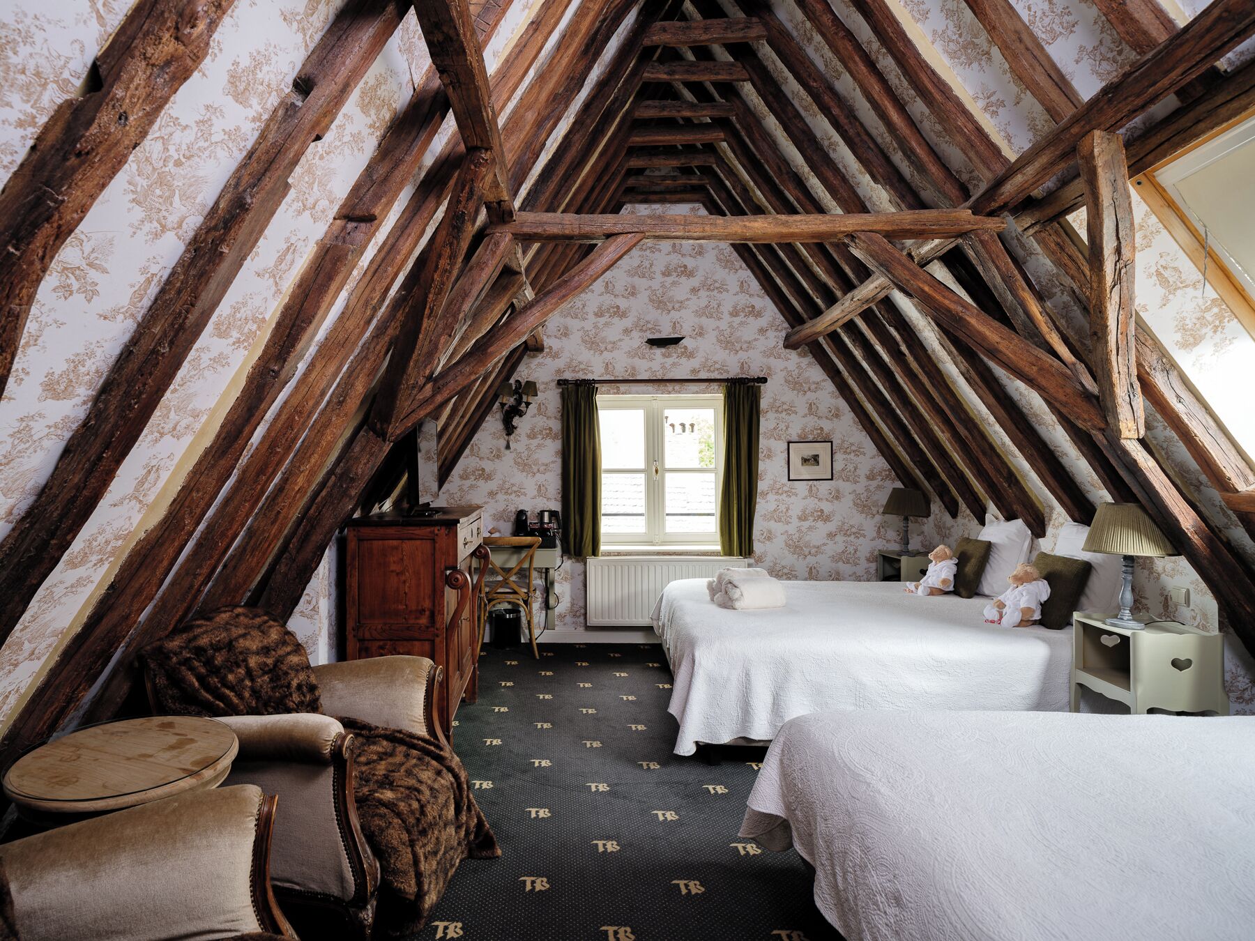 A cozy attic bedroom with exposed wooden beams, a bed, a chair, a dresser, and a window with curtains.