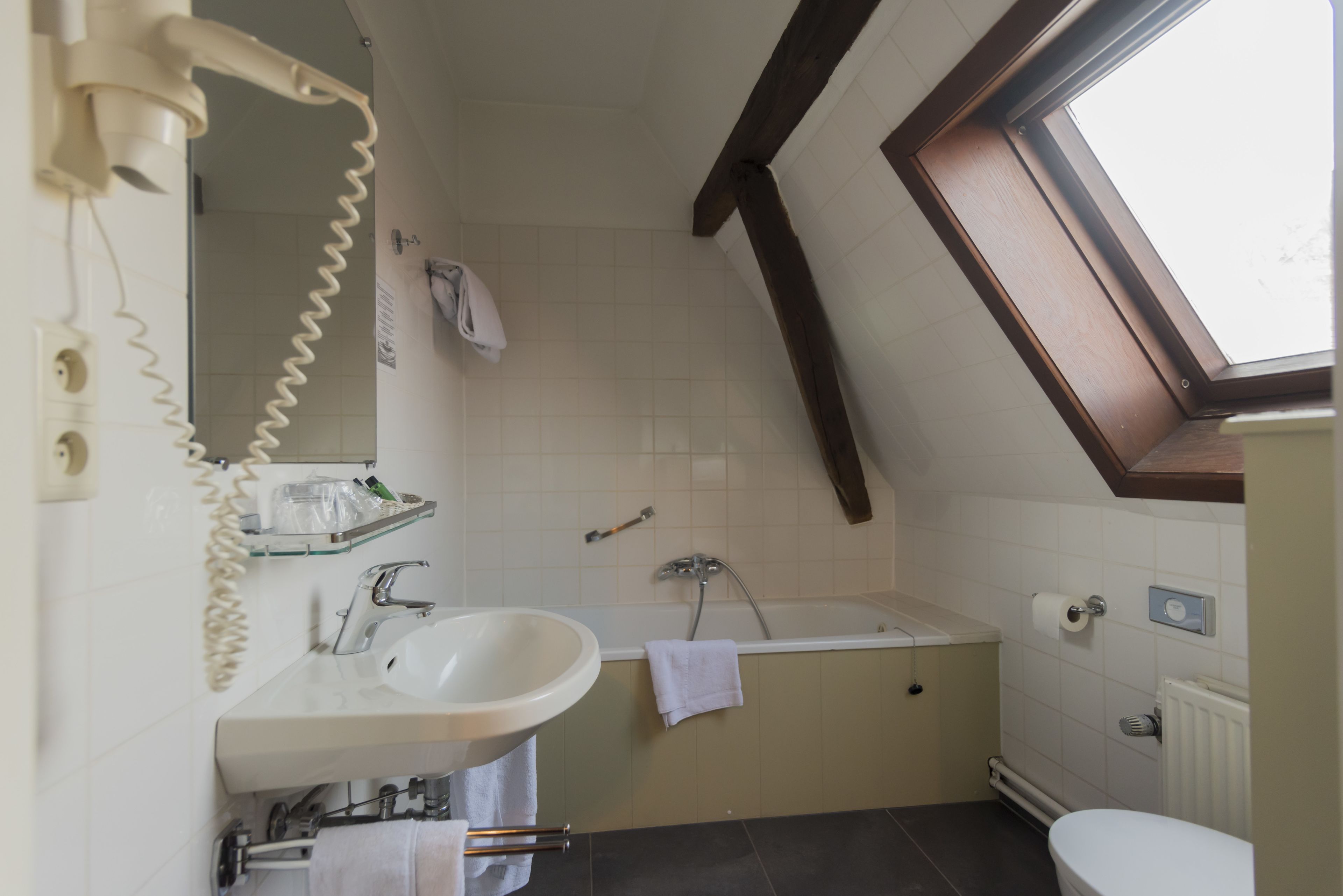 A bathroom with a sink, mirror, towel rack, and a window above the bathtub.