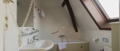 A bathroom with a sink, mirror, towel rack, and a window above the bathtub.