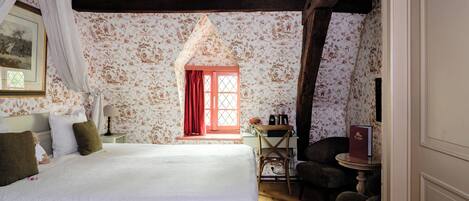 Una camera da letto con un letto grande, una sedia di legno, un tavolino e una finestra con tende rosse.