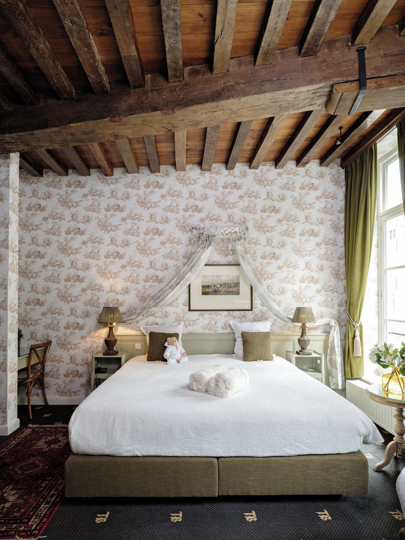 A bedroom with a large bed, floral wallpaper, a canopy, and a view of the outside through a window.