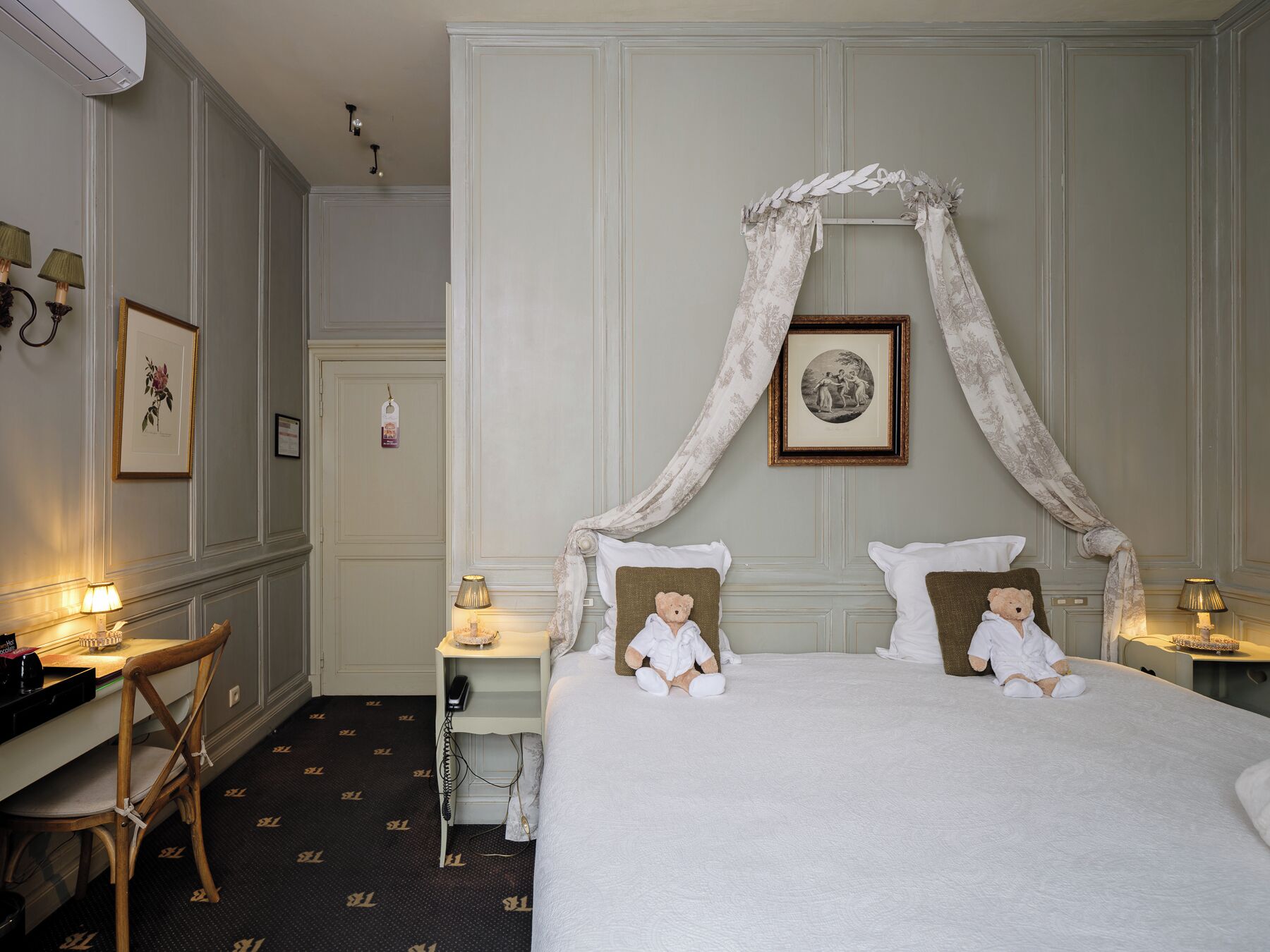 A hotel room with a large bed, two bedside tables with lamps, a chair, a desk, and a wardrobe.