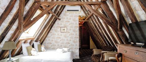 A cozy attic bedroom with exposed wooden beams, a bed, a dresser, and a television.