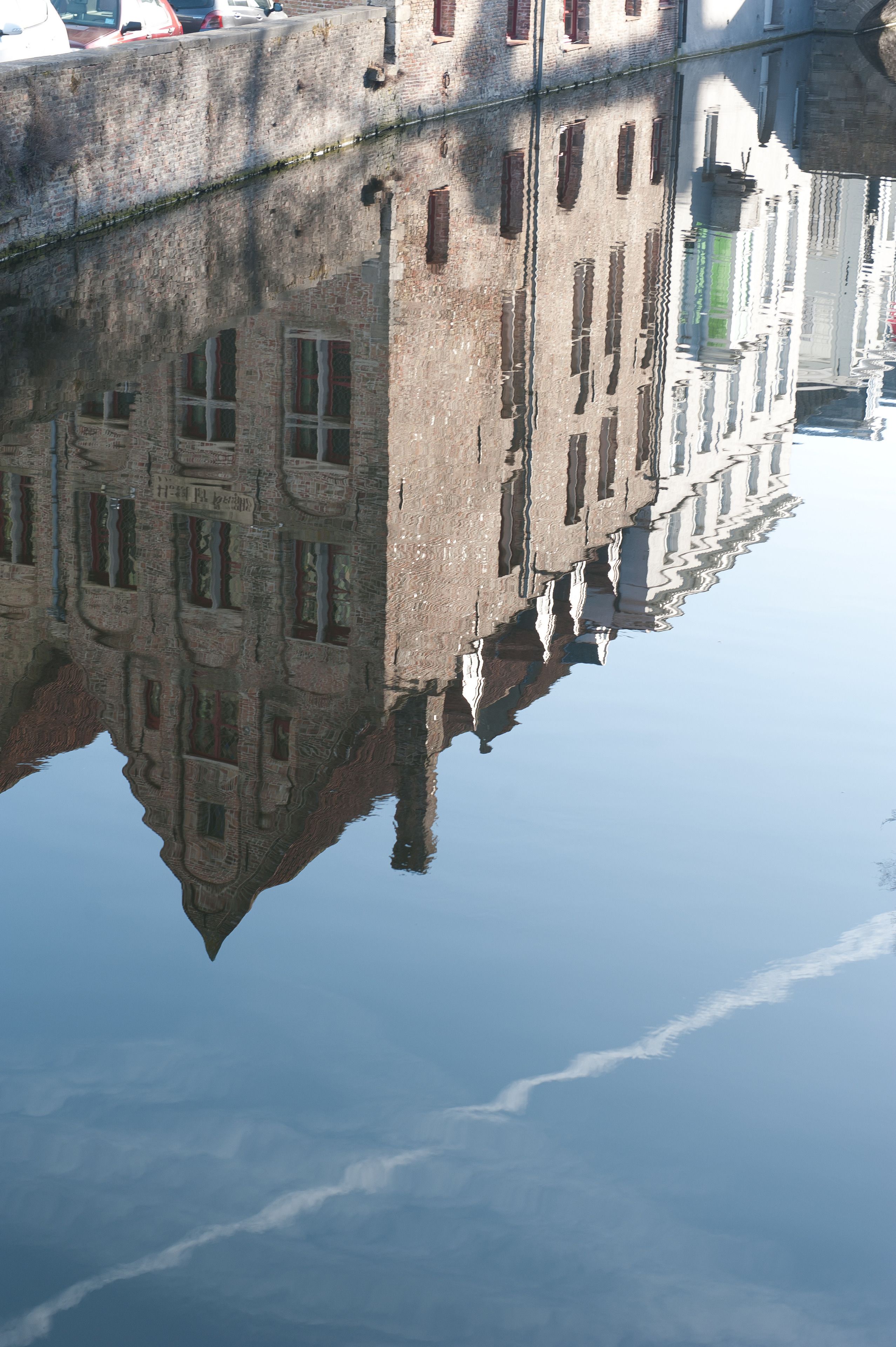 Un bâtiment se reflétant dans une étendue d’eau calme, avec de nombreuses fenêtres et une façade en briques.