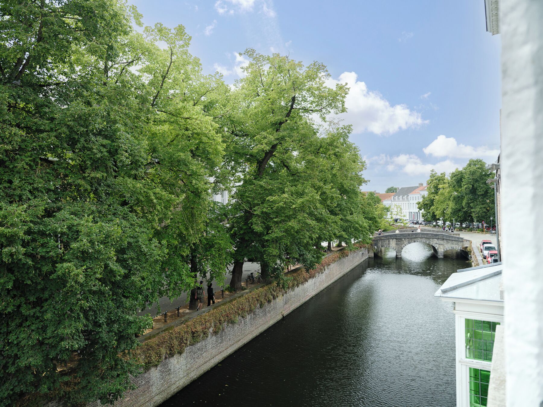 Un canale con un ponte di pietra, fiancheggiato da alberi e da un marciapiede.