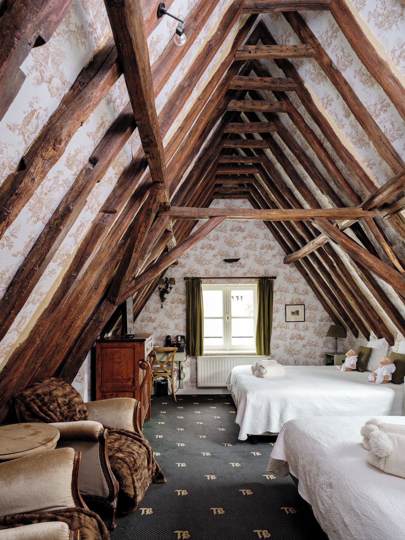 Um quarto de sótão aconchegante com vigas de madeira aparentes, uma cama, uma cadeira e uma pequena escrivaninha.