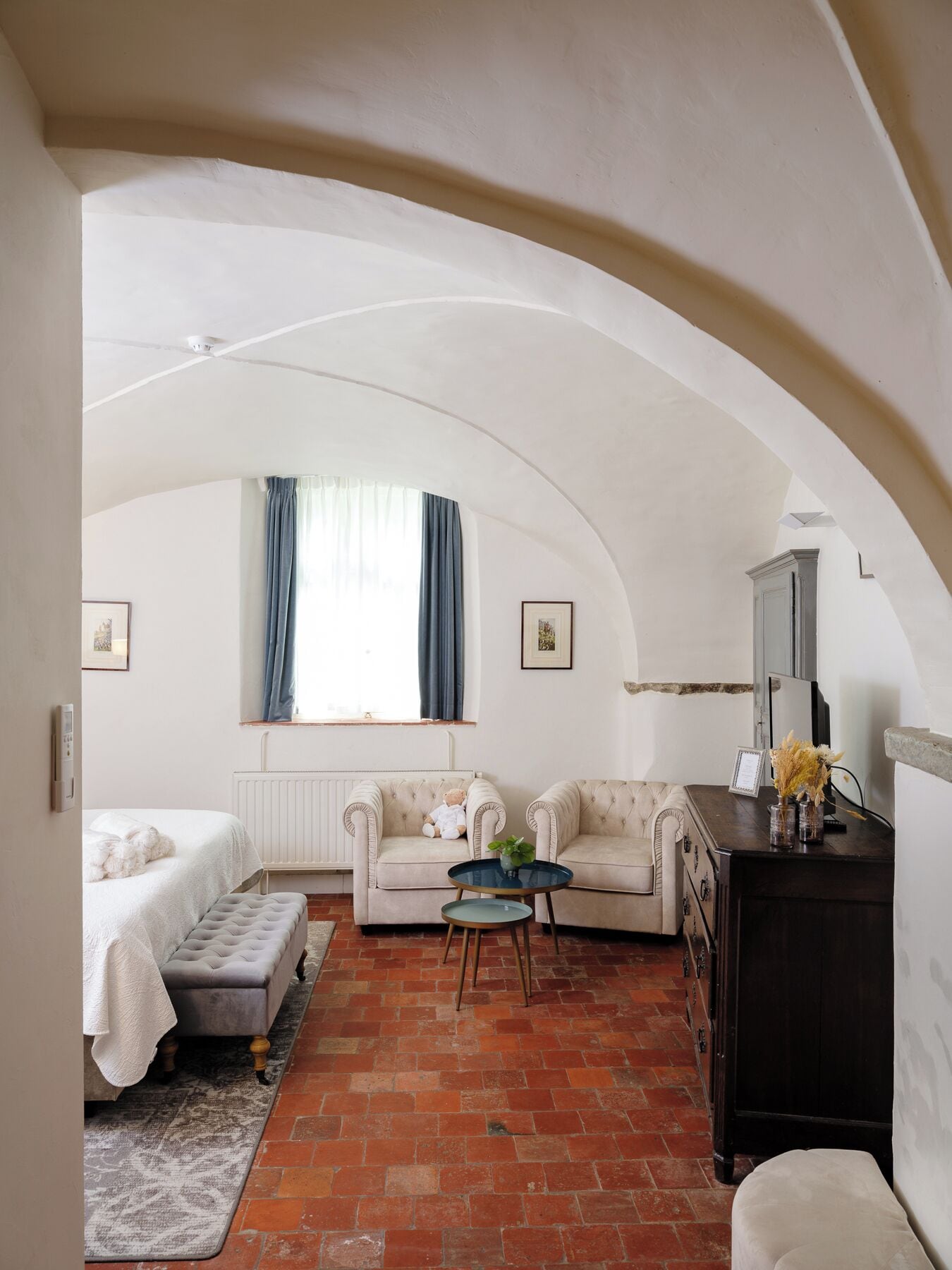 A cozy room with a vaulted ceiling, a bed, a sofa, a small table, and a dresser.