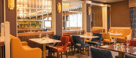 Ein Restaurant mit Barbereich, verschiedenen Sitzmöglichkeiten, darunter Sitzecken und Tische, und einer Wandgestaltung mit Muster.