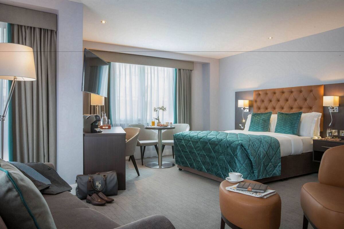A hotel room with a large bed, a desk with a chair, a small table with a vase, and a sofa.