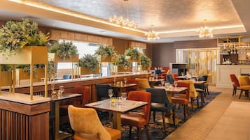 En restaurang med flera bord och stolar, en bardisk och dekorativa växter.