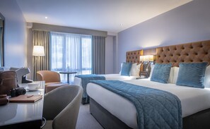 A hotel room with a large bed, a desk with a chair, a lamp, and a window with curtains. - Grand Canal Hotel Dublin (Dublin)