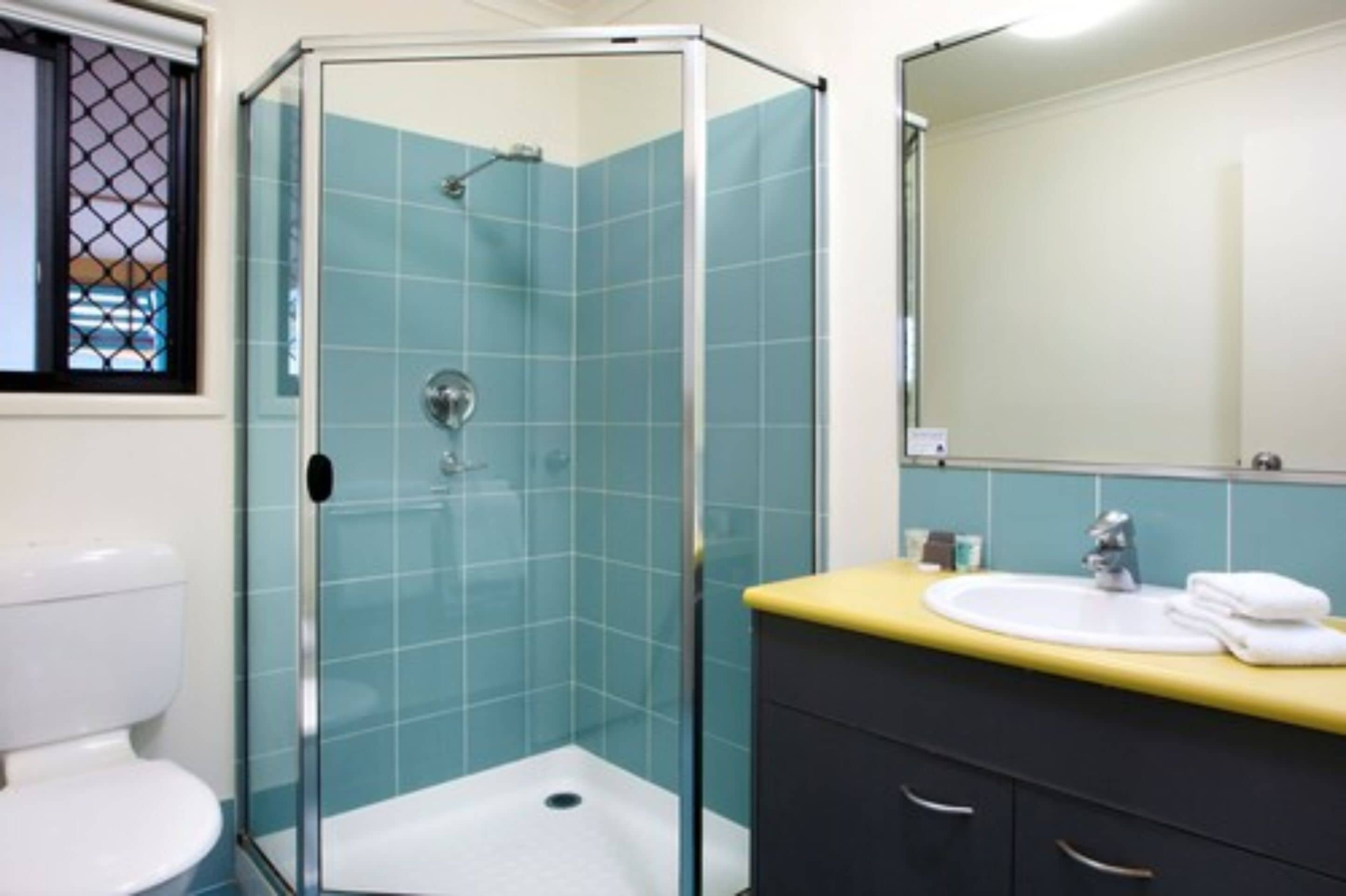 A bathroom with a glass-enclosed shower, a white toilet, a sink with a yellow countertop, and a mirror above the sink.