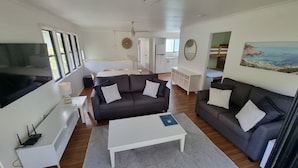 A modern living room with a grey sofa, a white coffee table, and a TV on the left. There is a painting of a coastal scene on the right wall.