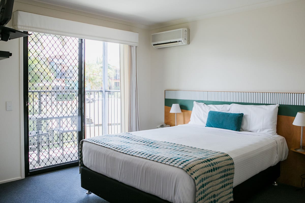 Une chambre d’hôtel comprenant un lit, une table de chevet, une lampe, une fenêtre avec vue et un appareil de climatisation.