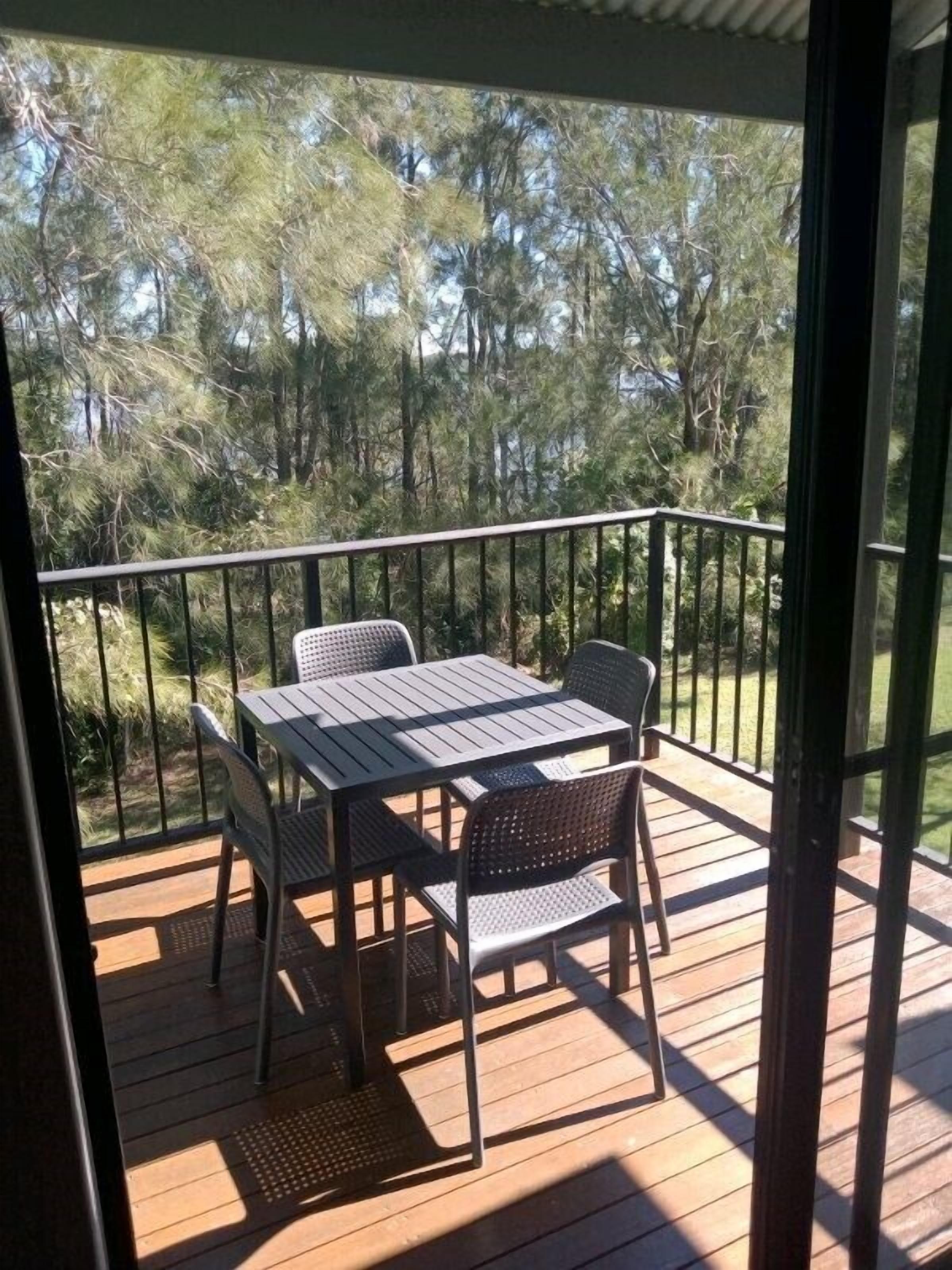 A wooden deck with a table and chairs, surrounded by a metal railing, overlooking a forested area.