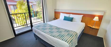 A hotel room with a large bed, a nightstand, a lamp, and a sliding glass door leading to an outdoor area.