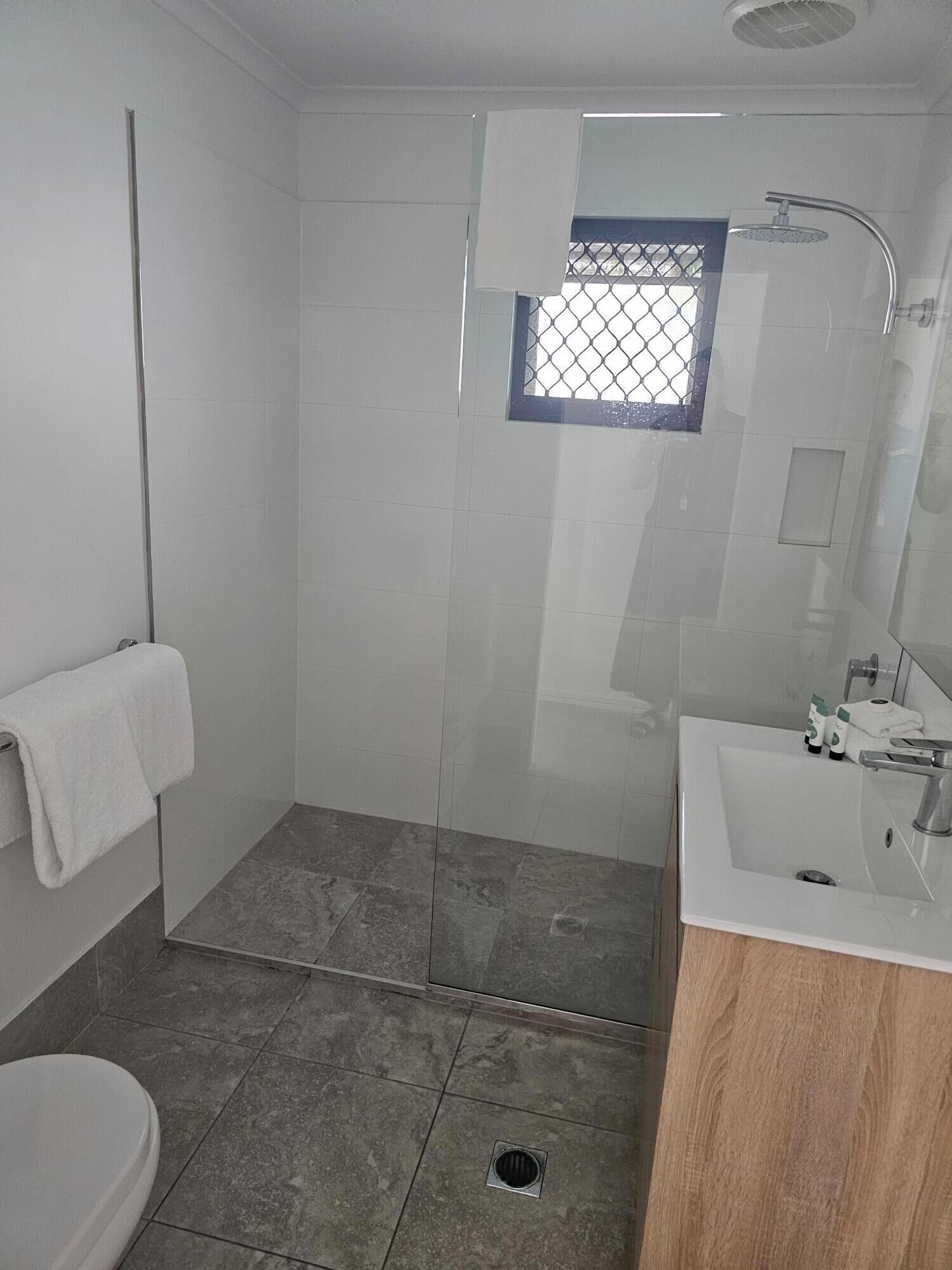 A modern bathroom with a glass-enclosed shower, a white sink, and a toilet.