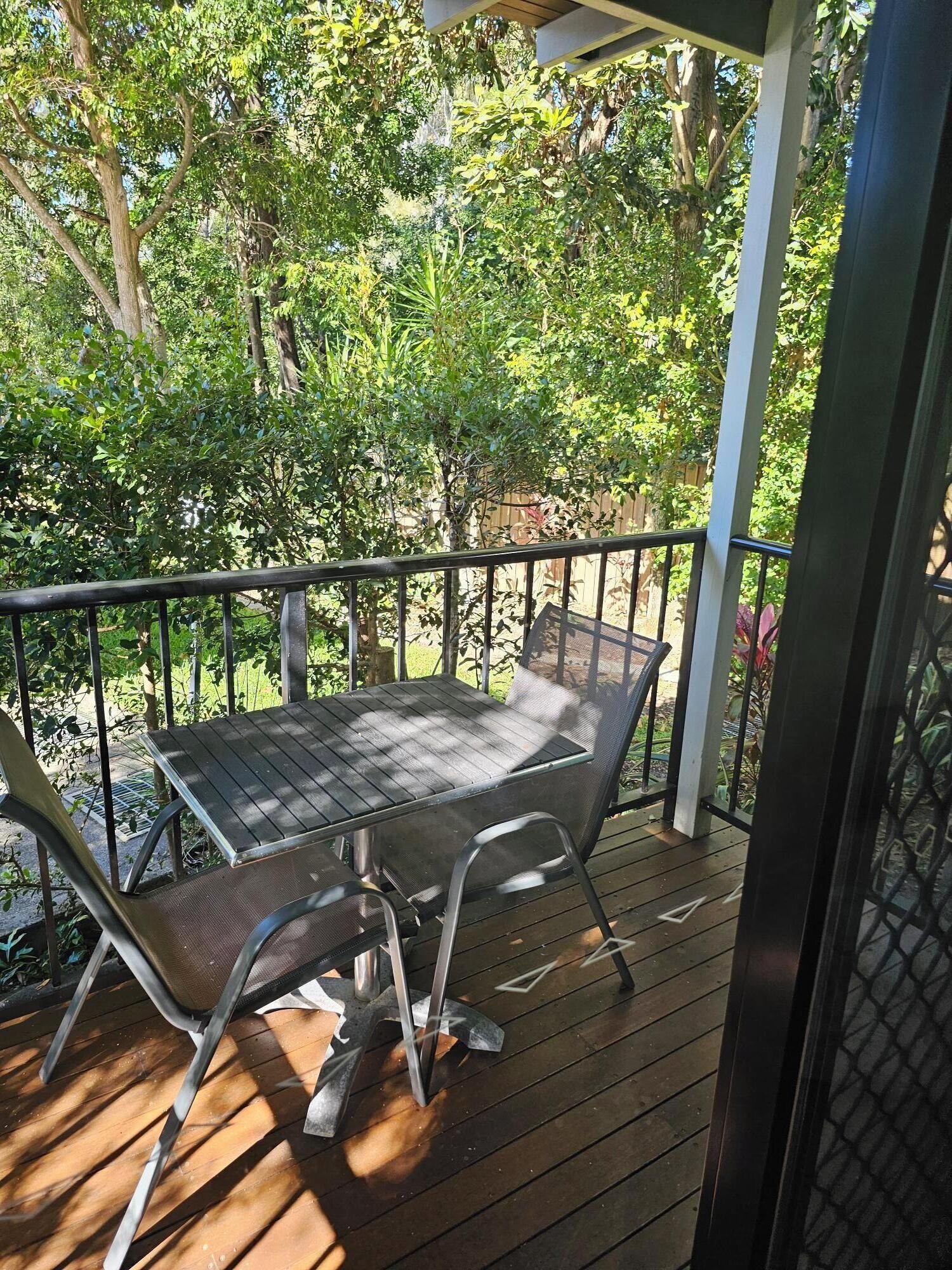 A wooden deck with a metal table and chairs, surrounded by lush greenery and trees.