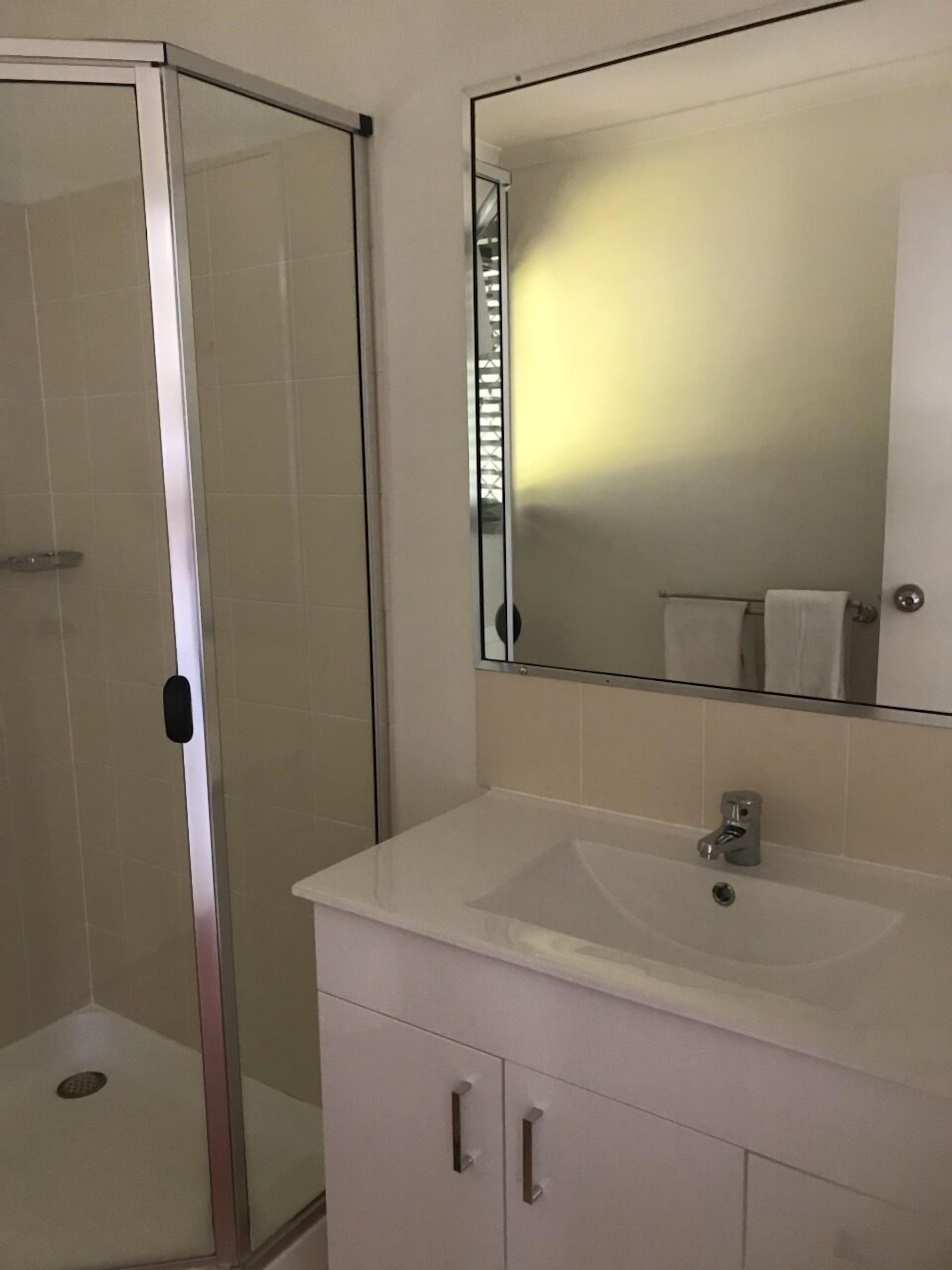 Un baño con cabina de ducha de vidrio, un lavabo blanco y un espejo sobre el lavabo.