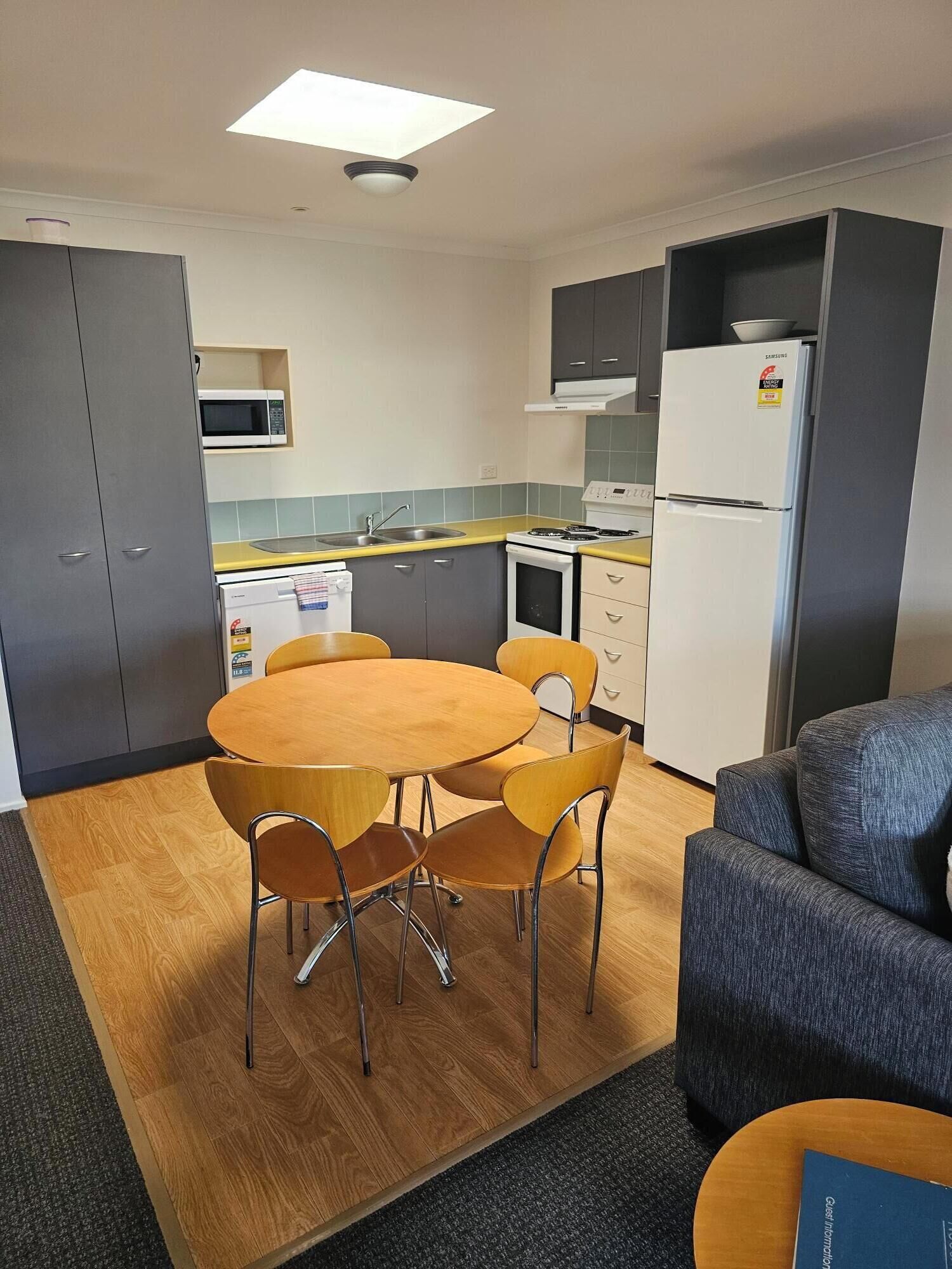 Une cuisine compacte équipée d’un four à micro-ondes, d’une cuisinière et d’un réfrigérateur. On y trouve une table à manger avec des chaises et un canapé.