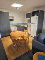 Cocina compacta equipada con microondas, estufa y refrigerador. Incluye una mesa de comedor con sillas y un sofá.