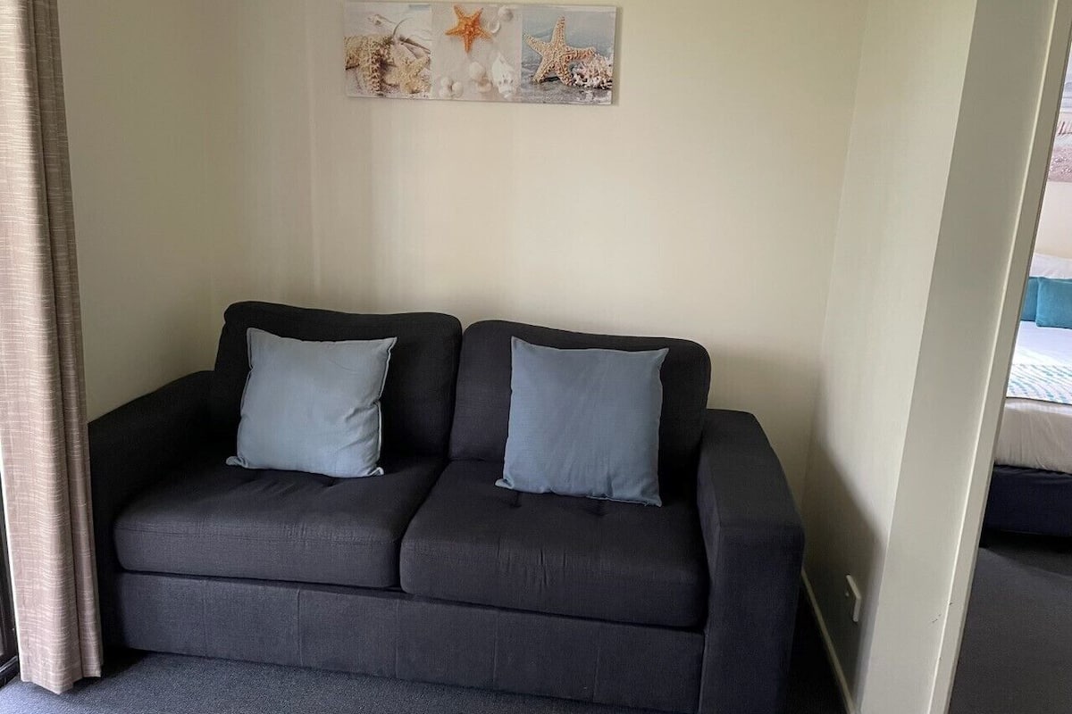 Un canapé gris foncé agrémenté de deux coussins assortis, dans une pièce dont le mur est peint dans une couleur claire.