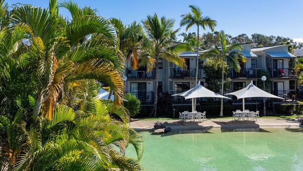 A resort with a pool, outdoor seating, and palm trees.
