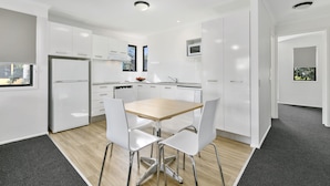 A modern kitchen with white cabinetry, a wooden table, and two white chairs.