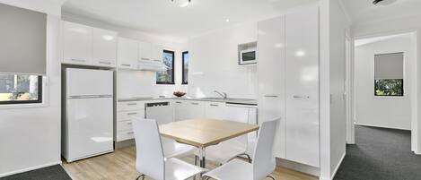 A modern kitchen with white cabinetry, a wooden table, and two white chairs.