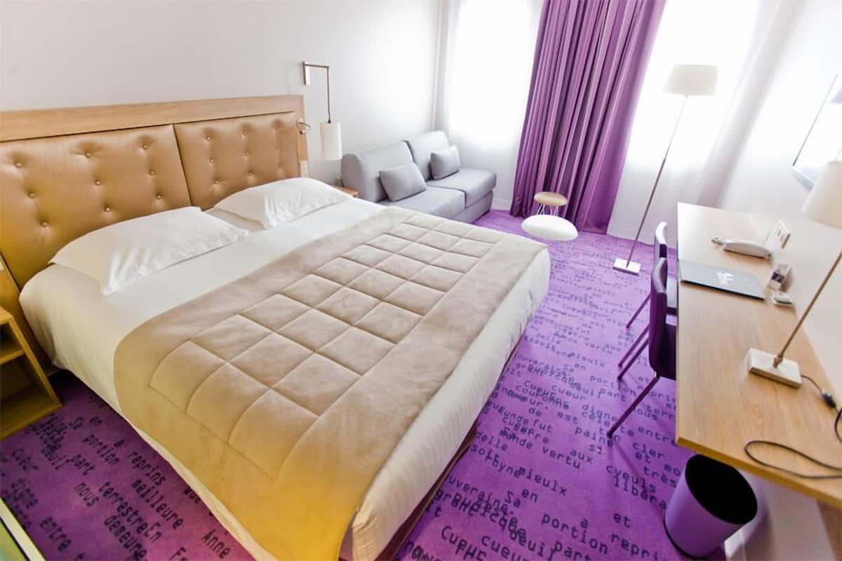 A hotel room with a large bed, a sofa, a desk, and a chair.