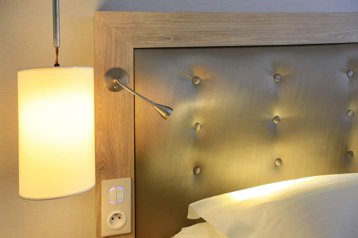 A bed with a headboard featuring a tufted design and a wall-mounted light fixture.