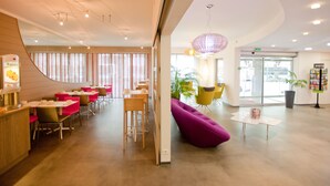 A modern hotel lobby with a curved reception desk, multiple dining areas with red and yellow chairs, and a purple seating area. - Hotel Anne de Bretagne (Rennes)