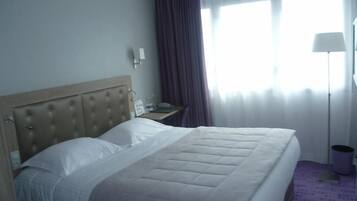 Una habitación de hotel con una cama grande, una mesita de noche, una lámpara y una ventana con cortinas.