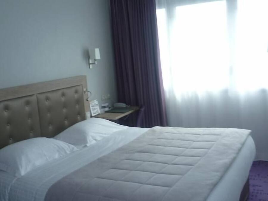 Una habitación de hotel con una cama grande, una mesita de noche, una lámpara y una ventana con cortinas.