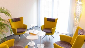 A modern room with yellow chairs, a small table, and a large window. - Hotel Anne de Bretagne (Rennes)