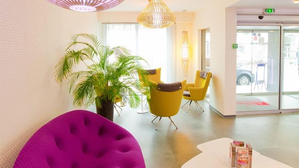 A modern lobby with a purple bean bag chair, yellow chairs, and a white table with magazines. - Hotel Anne de Bretagne (Rennes)