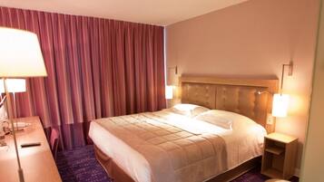 A hotel room with a large bed, two bedside lamps, a desk with a lamp, and a curtain.