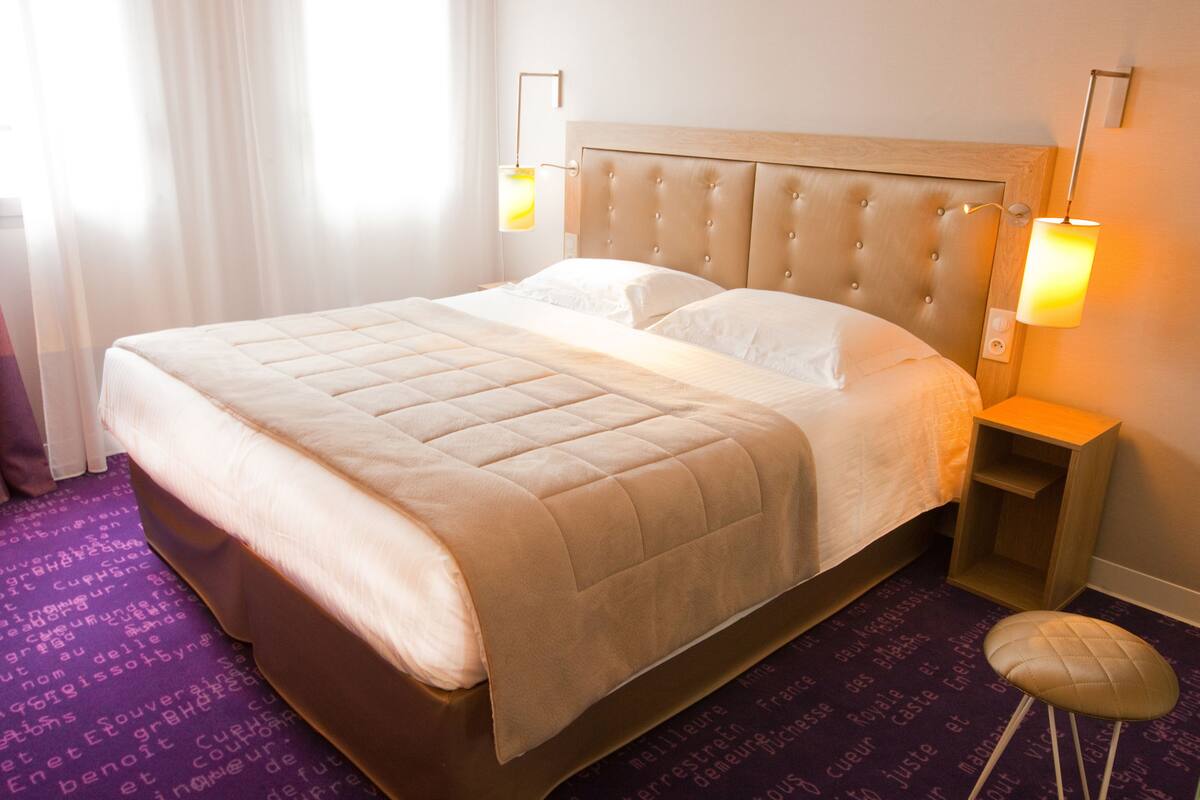 A hotel room with a large bed, two bedside lamps, and a purple carpet with text.