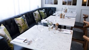 A dining area with a black leather sofa, marble tables, and wooden chairs. - The Fox & Goose Hotel (London)