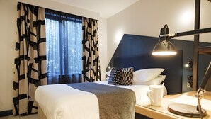 A hotel room with a bed, a desk with a lamp, a coffee cup, and a window with curtains. - The Fox & Goose Hotel (London)