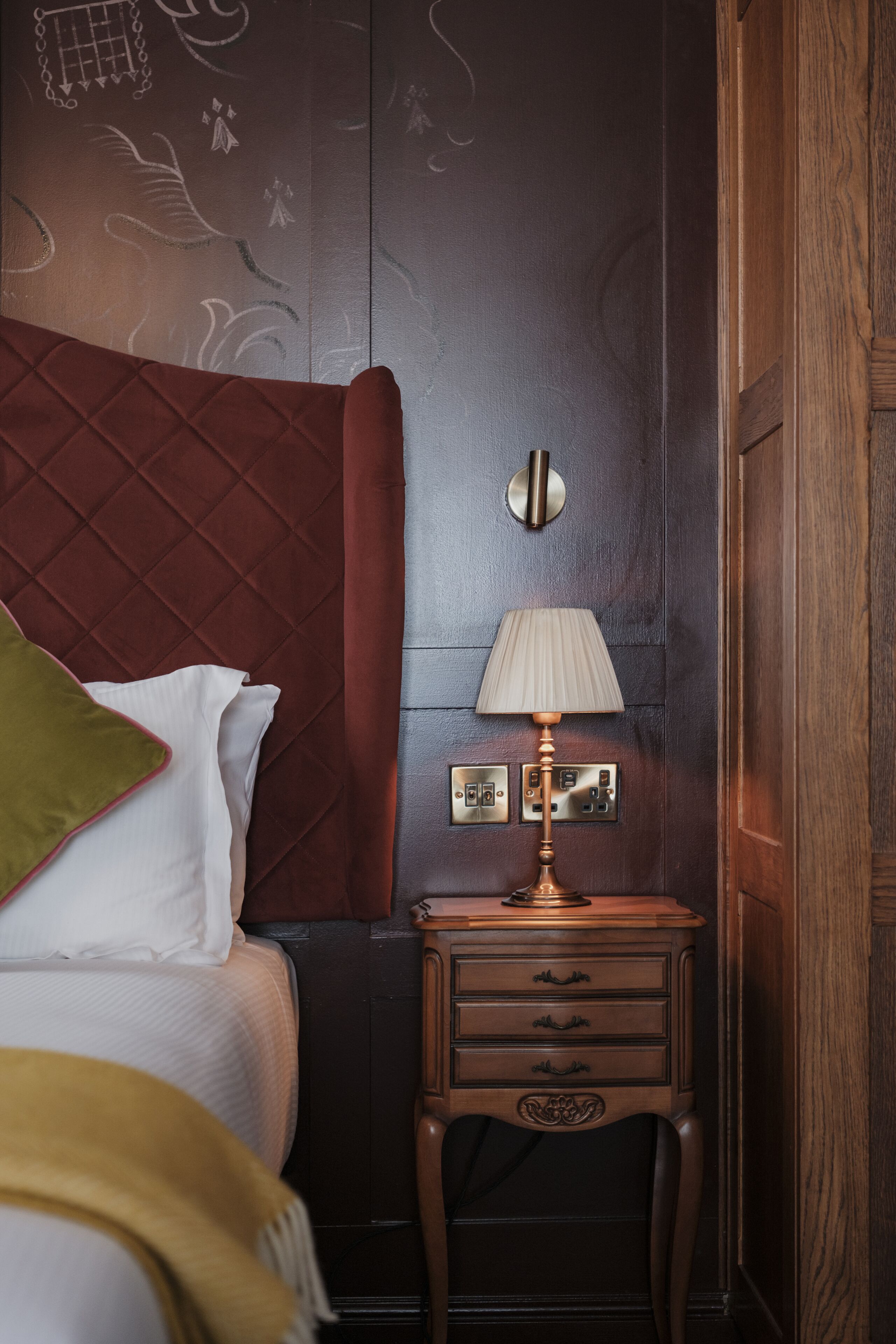 Una habitación de hotel con una cama, una mesita de noche con lámpara y un muro con paneles decorativos.