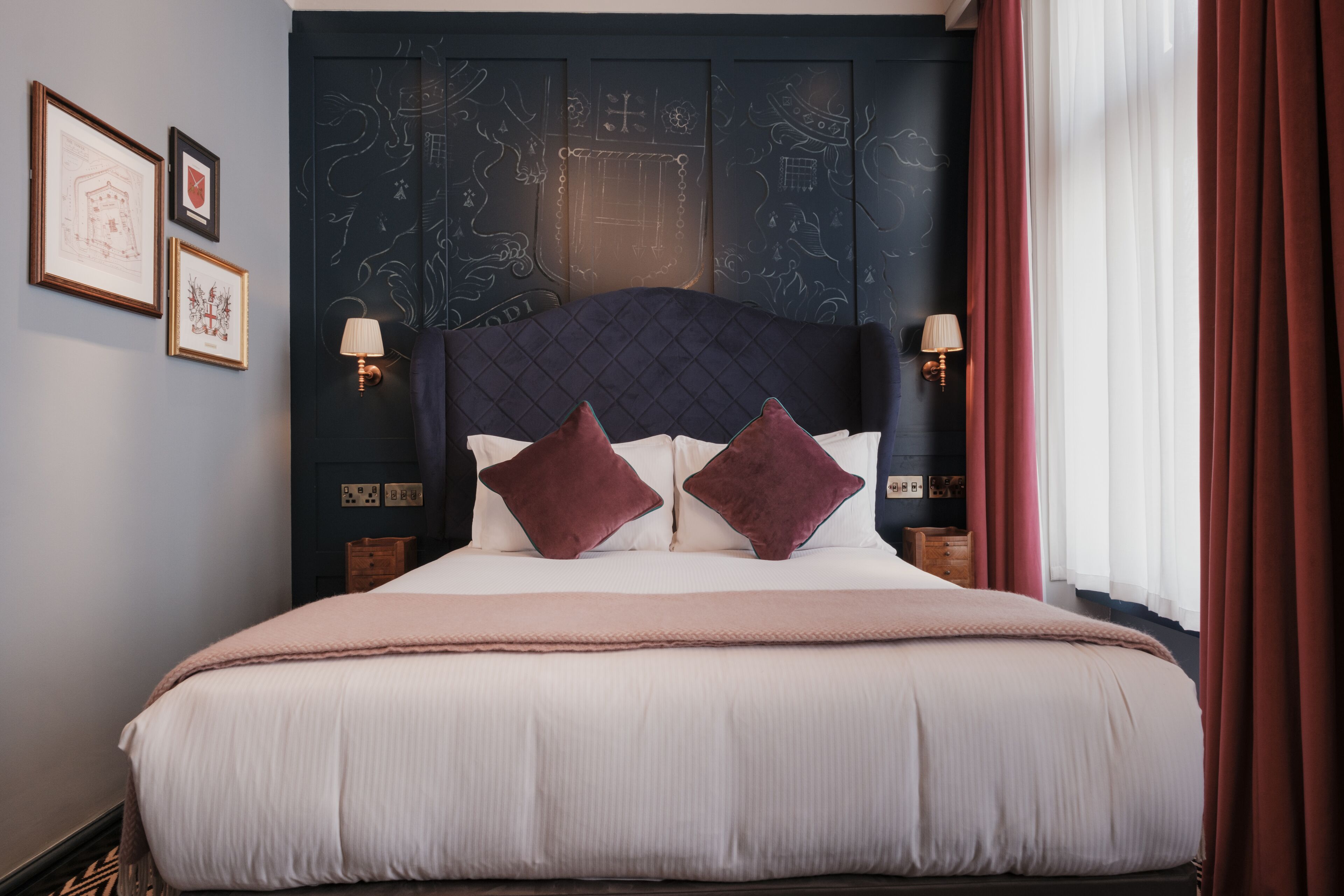 A neatly made bed with a quilted headboard, two bedside lamps, and a window with curtains.