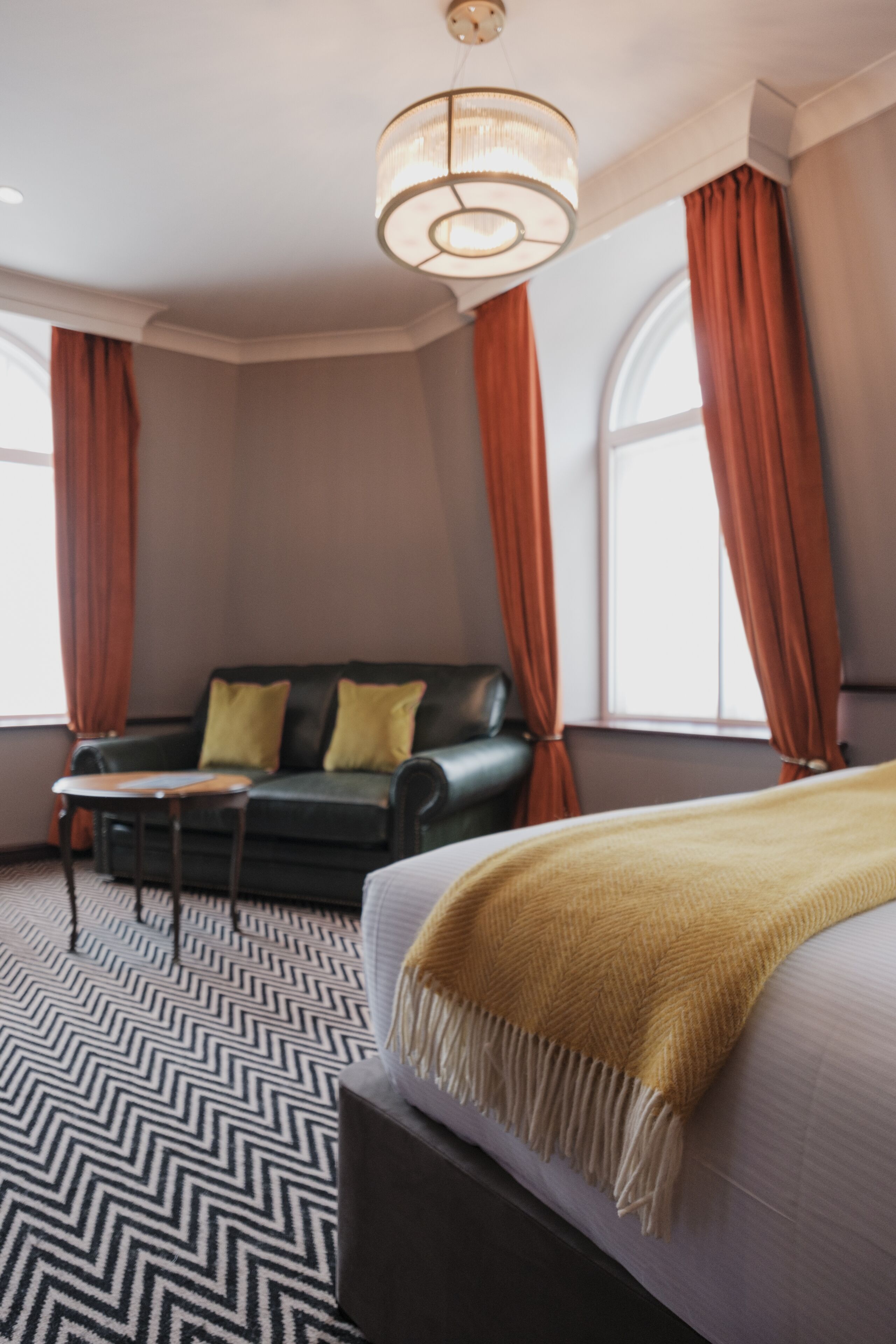 A hotel room with a bed, a sofa, a table, and a chandelier.