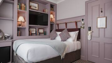 Un dormitorio con cama, estanterías empotradas con libros y televisor, una puerta con cerradura y suelo estampado.