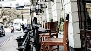 A row of wooden tables and chairs outside a building with a white facade and black railings. - The Mad Hatter Hotel (London)